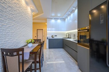 Geniş lüks, beyaz ve koyu gri mutfak. Yemek masası var.