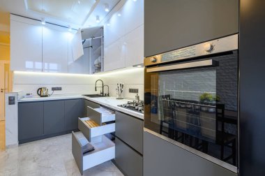 Geniş lüks, beyaz ve koyu gri, modern mutfak. Yemek masası, mobilya çekmeceleri ve kapıları açık.