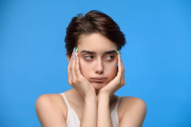 Depressed and pouting sensual young teenage girl looking sideways, at blue background