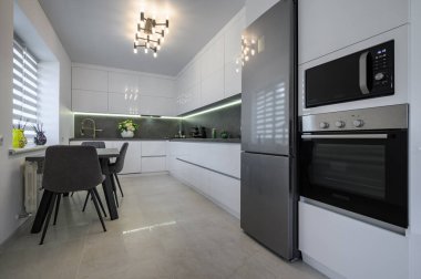 Luxurious modern trendy white and grey kitchen interior after renovation, with granite counter top and marble floor, dining table next to window