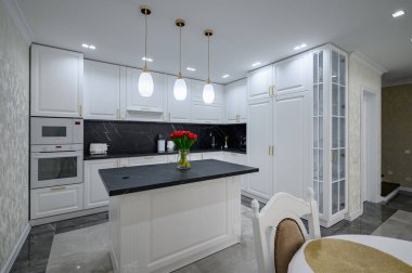 Luxurious white large modern domestic kitchen with black marble worktop and serverd dining table
