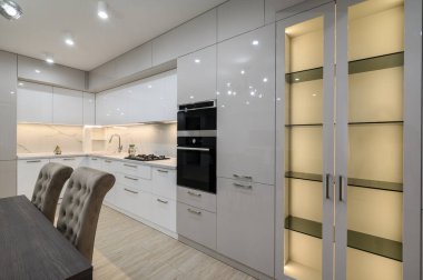 Yemek masası ve sandalyeler, beyaz ferah döşeli mutfak içi fırın ve sağ tarafta büyük LED aydınlanmış büfe.