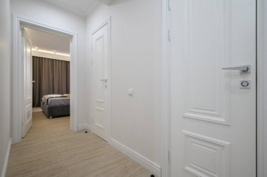 Beyaz koridor, arka planda yatağı olan bir yatak odası var.