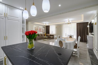 Lüks, beyaz, büyük, modern bir stüdyo. Mutfak masasının üzerinde siyah mermer tezgah var.