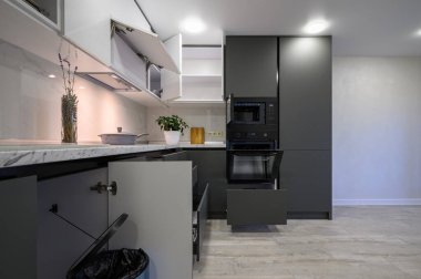 Modern, basit, koyu gri ve beyaz mutfağın iç mekanı. Çekmeceler geri çekilir, kapılar açılır.
