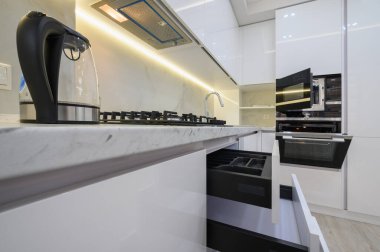 Sobası, fırını ve açık kapılı mikrodalgası olan beyaz modern mutfak, atölyede cam elektrikli su ısıtıcısı, çekmeceler geri çekiliyor.