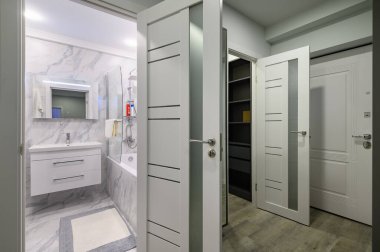 Küçük modern oturma odasına bağlı giriş salonu, banyoya ve savaş alanına açılan kapılar açık.