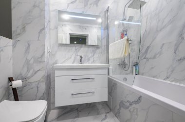 Klozet kapağı, gösterişli ayna ve küveti olan modern beyaz mermer banyo.