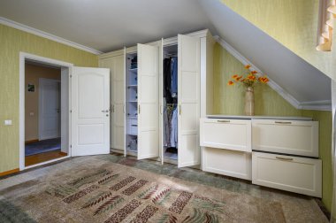 Geniş yatak odasının içi kırsal tarzda. İçerisinde açık kapılar ve çekmeceler olan büyük duvarlı gardıroba bakın