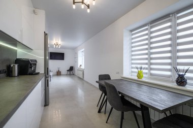 Luxurious modern trendy white and grey kitchen interior after renovation, with granite counter top and dining table next to window