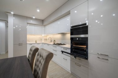 Duvarında televizyon olan büyük, beyaz, lüks bir stüdyo dairenin içinde büyük bir mutfak, bir sürü fotokopi alanı, sandalyeli yemek masasının yakın görüntüsü.