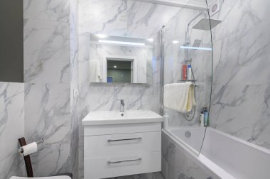 Dolap, makyaj aynası ve küveti olan modern beyaz mermer banyo.