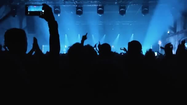 不知名的歌迷在音乐会或节庆晚会上跳舞和举手 观众在明亮的舞台灯光前欣赏音乐会的剪影 — 图库视频影像