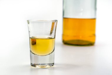 Bardakta alkol, beyaz masanın arkasında da bir şişe brendi. Alkol zehirlenmesinden. Alkol bağımlılığı kavramı. Alkol zehirlenmesi.
