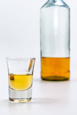 Bardakta alkol, beyaz masanın arkasında da bir şişe brendi. Alkol zehirlenmesinden. Alkol bağımlılığı kavramı. Alkol zehirlenmesi.