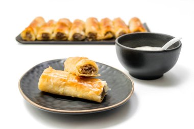 Etli börek, oval bir tabakta yumurta dilimlenmiş domuz eti ve arka planda bir kase tartar sosu ve og ruloları, seçici odak, kırpma yolu dahil olmak üzere beyaz arka planda izole edilmiş..