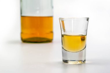 Bardakta alkol, beyaz masanın arkasında da bir şişe brendi. Alkol zehirlenmesinden. Alkol bağımlılığı kavramı. Alkol zehirlenmesi.
