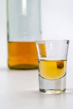 Bardakta alkol, beyaz masanın arkasında da bir şişe brendi. Alkol zehirlenmesinden. Alkol bağımlılığı kavramı. Alkol zehirlenmesi.