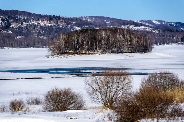 stock image Winter landscape with a tributary River entering the frozen lake with with lake island and hills in the background background. Frozen Lake on a cold winter day.