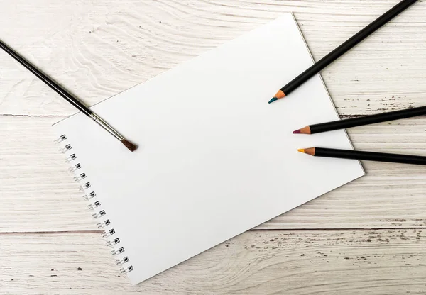 白纸和彩色铅笔在白色木制背景上作画的笔记本 — 图库照片