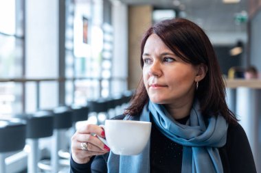 Kafeteryada elinde kahve fincanı tutan düşünceli olgun bir kadın. Orta yaşlı kadın düşünürken çay içiyor. Kahve içerken rahatlamak ve düşünmek..