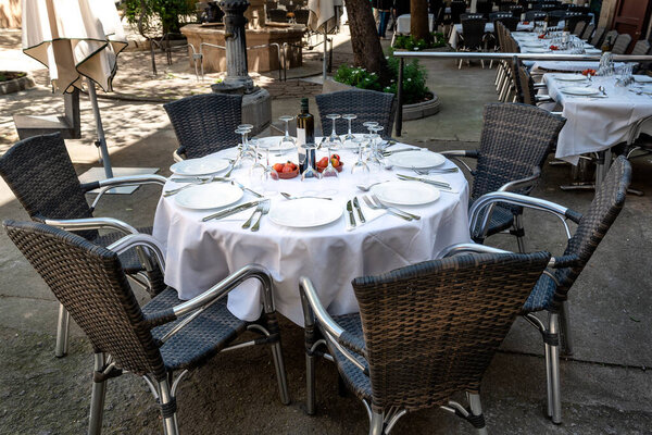 Empty outdoor restaurant table set for dinner with dishes, utensils and wine glasses