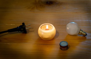 Saving electricity concept. Electric bulb and cable plug with candle on a wooden table. Eugo coins. Symbol of return to the past. Incandescent bulb and candle. Power cut or power outage. High electricity prices. clipart