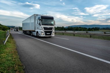 Büyük kamyonlar gün batımında ormanlık alanda otoyolda ilerliyorlar..