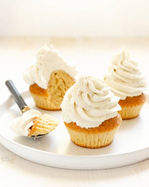 Beyaz bir tabakta vanilya tohumlu lezzetli kremayla süslenmiş nemli vanilyalı kekler ve beyaz ahşap bir arka planda, yukarıda yazı için yer var..