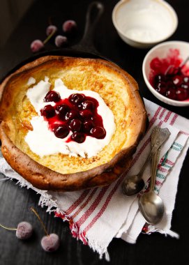 Vişne soslu Hollanda bebek krepi ve siyah bir masada tavada yoğurt.