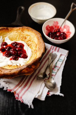Vişne soslu Hollanda bebek krepi ve siyah bir masada tavada yoğurt.