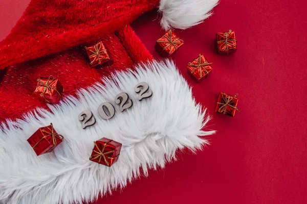 Kırmızı arka plandaki Noel Baba şapkasında hediyeler ve 2022 numaralar var.