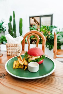 Vejetaryen burger, kırmızı çörek, patates kızartması, yeşil tabak, ahşap masa, sağlıklı vejetaryen yemeği..