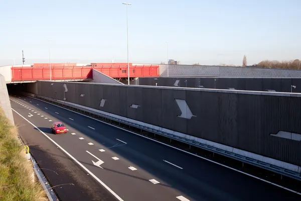 Czerwony samochód opuszcza tunelu na autostradzie w Holandii — Zdjęcie stockowe