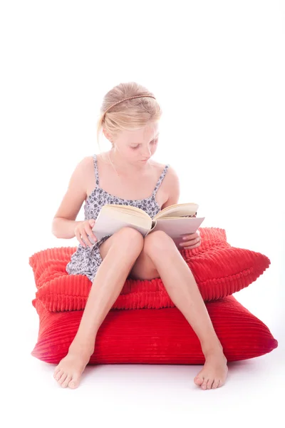 Girl reads a book on red cushions — Stock Photo, Image