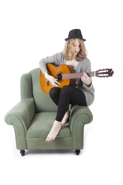 Mladá krásná žena hrající kytaru na straně křesla — Stock fotografie