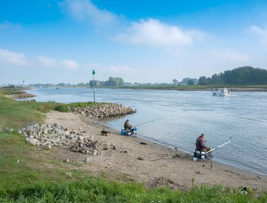 two men fishing on embankment of river ijssel in the netherlands under blue sky clipart