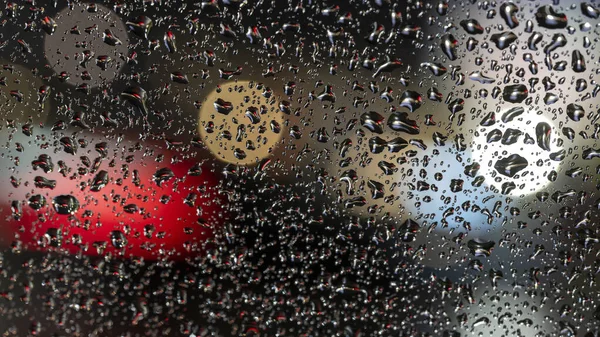 Luzes não afiadas difusas coloridas atrás da janela de vidro com gotas de chuva — Fotografia de Stock