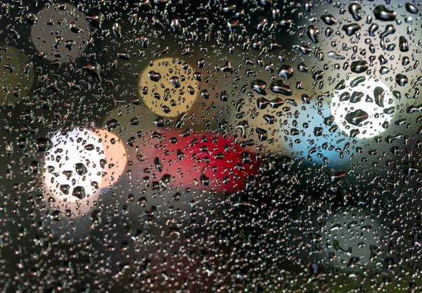 Kolorowe rozproszone nieostre światła za szybą z kroplami deszczu — Zdjęcie stockowe