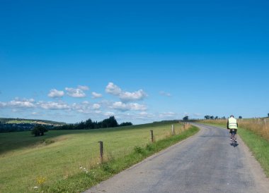 Bisikletli bir adam Belçika 'nın kırsal kesimindeki tepeye tırmanır Han sur less ve Rochefort yakınlarında yazın mavi gökyüzünün altında.