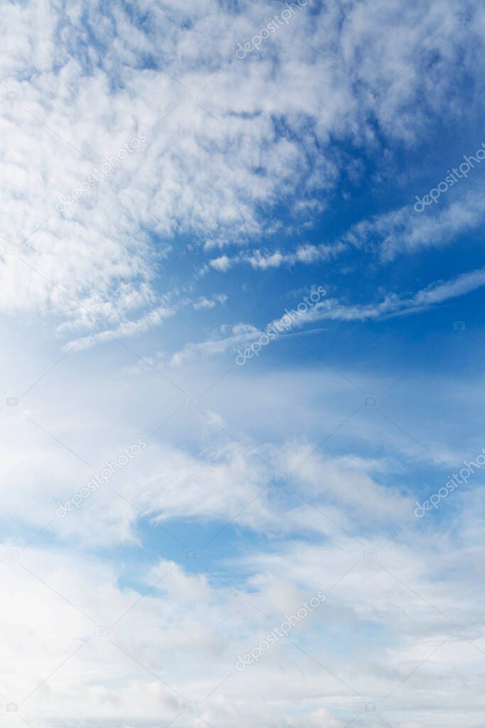 A clear blue sky with cirrus clouds and chemtrail stripes. Background. Space for text. Vertical.