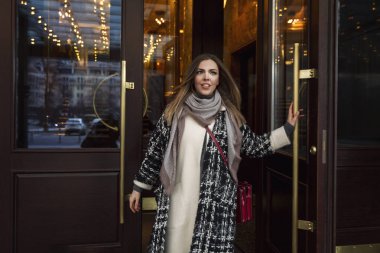 Genç, gülümseyen bir kadın şık, güzel bir binanın kapısını açar. Şık ceketli güzel sarışın..