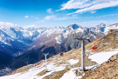 Açık güneşli bir günde kar kaplı dağlarda mavi bulutlu bir gökyüzünün zeminine karşı kaldırma mekanizması olan kablo araba. Aktif eğlence ve kış sporları. Dombay, Rusya, 10-31-2021.