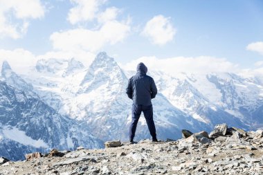 Bir adam karlı dağlarda durur ve muhteşem manzaraya hayran kalır. Aktif turizm, yürüyüş ve kış sporları. Arka plan.