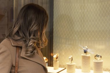 Genç ve zarif bir kadın pahalı bir saati olan bir vitrine bakıyor. Mücevher ve aksesuarlar..