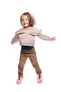 Küçük gülen kız atlıyor. Kahverengi kotlu ve pembe kazaklı bir çocuk. Özgürlük, mutluluk ve olumluluk. Beyaz arka planda izole edilmiş. Dikey.