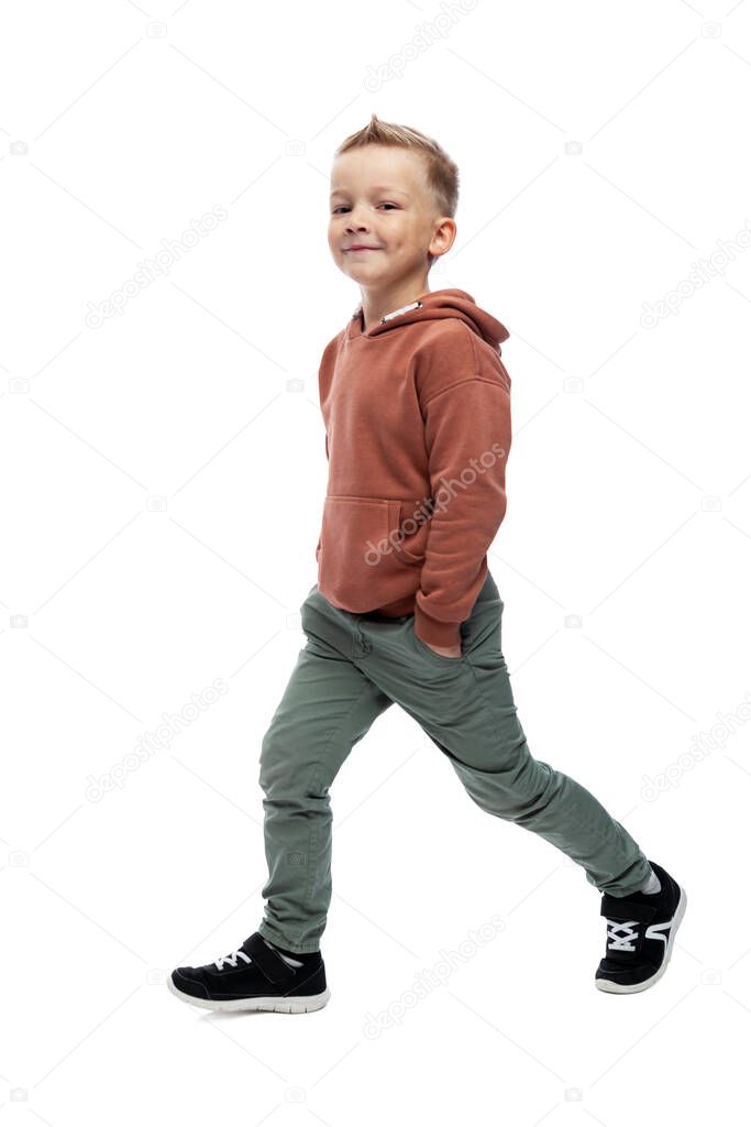The smiling boy is walking. Preschooler in gray jeans and a brown sweater. Positiveness and movement. Isolated on white background. Vertical.