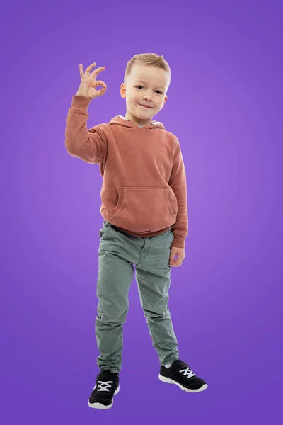 Pięcioletni Chłopiec Stoi Pokazuje Znak Ręką Dziecko Dżinsach Brązowy Sweter — Zdjęcie stockowe
