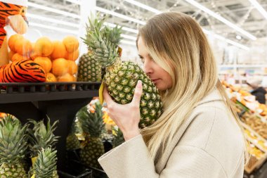 Genç bir kadın dükkanda ananas seçiyor. Sağlıklı yiyecekler ve diyet yemekleri. Yakın plan..