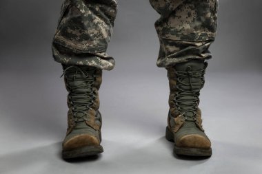 Kamuflaj kıyafeti ve asker botu giymiş bir adamın bacakları. Siyasi çatışmalar ve çalkantılı bir askeri ortam. Yakın plan. Gri arkaplan.